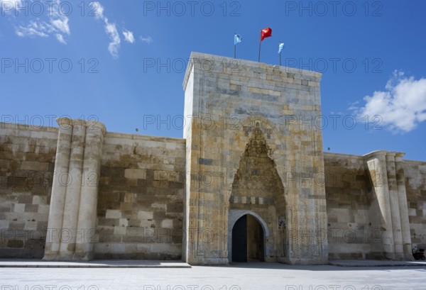 Historic fortress entrance with two flags under a cloudless sky, portal of the Sultanhani