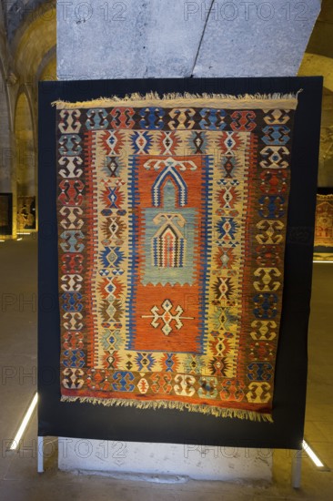 Colorful, traditional rug with detailed patterns displayed in a room, Sultanhani caravanserai, on