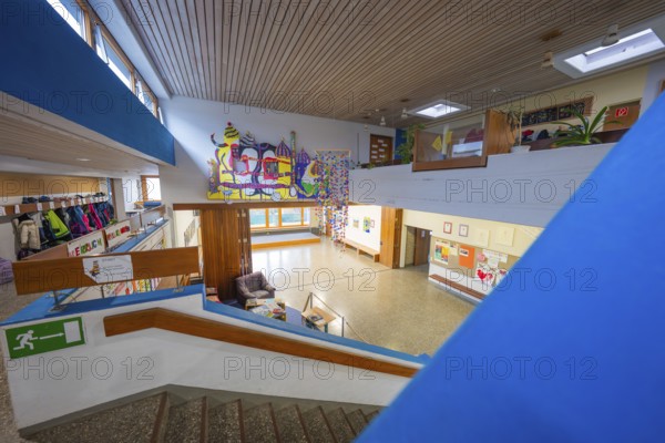 An interior with a staircase, decorated with art and a pleasantly illuminated wooden ceiling,