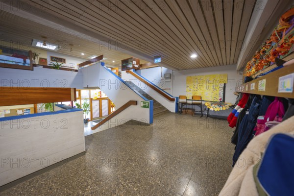 A bright corridor with cloakroom, colorful wall art and a modern wooden staircase, Schlehengäu