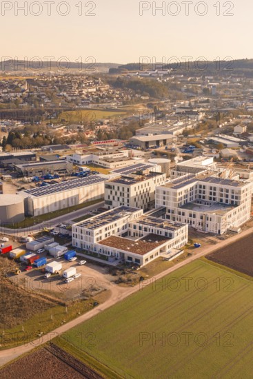 Aerial view of an industrial plant with modern buildings and surrounding fields in warm sunlight,