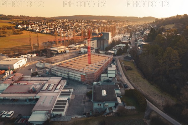 Urban scene with construction crane surrounded by residential areas and rolling hills at dusk,