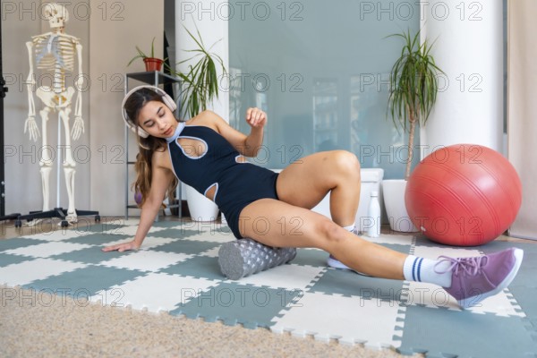 Young woman in activewear using a foam roller on a mat to perform self myofascial release for leg