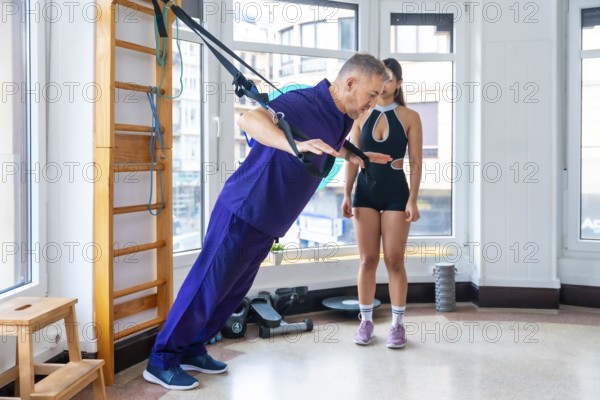 Physician assisting male patient performing strength exercises with suspension straps, guided by a