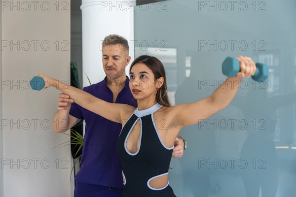 Young woman training with light dumbbells for sports recovery, guided by an experienced