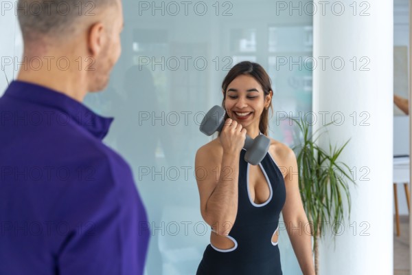 Smiling young woman doing biceps curls with a dumbbell under the guidance of a male