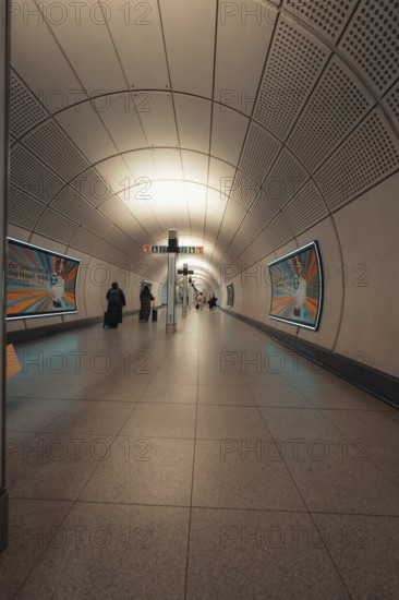 Modern subway tunnel with few passers-by and posters on the walls, London, Great Britain