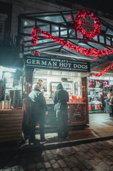 Market stall at night, decorated with Christmas lights, with people in front of it, London, Great