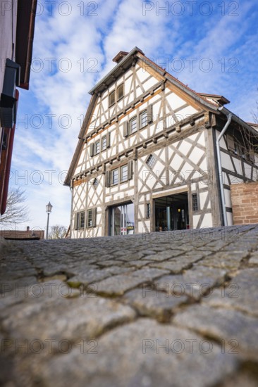 Timbered house with steep roof line against blue sky and cobblestone road, Ötisheim, Enzkreis,