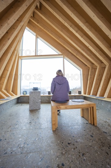 Person sitting on a bench in a modern wooden room with window view, Sinnraum, Oberreute, Allgäu,
