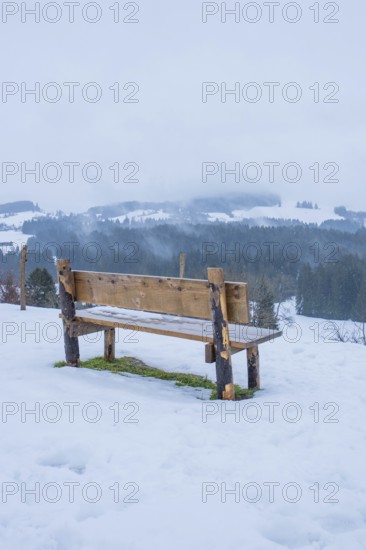 Wooden bench on snowy ground with a view of a quiet winter landscape, Sinnraum, Oberreute, Allgäu,