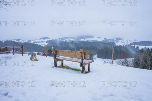 Wooden bench on snow-covered ground with view of winter landscape, Sinnraum, Oberreute, Allgäu,