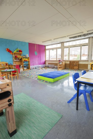 Bright kindergarten room with colorful walls and toy shelves, daylight through large windows,