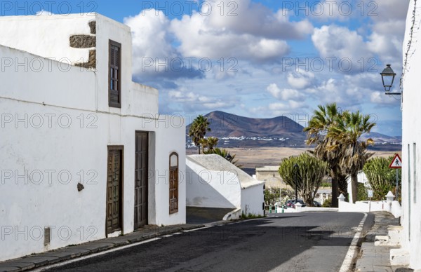 Typical white houses with colored doors and windows in an alley with volcanic craters behind,