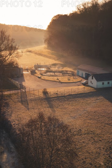 Sewage treatment plant at sunrise in a meadow with long shade, surrounded by trees and fog,