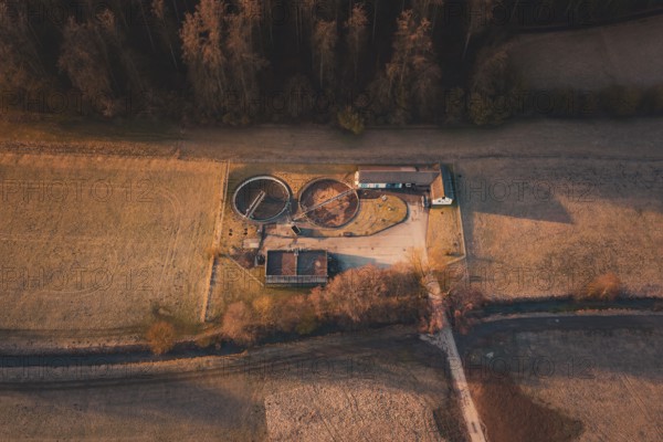 Sewage treatment plant with round basins and buildings in the midst of a wide field landscape with