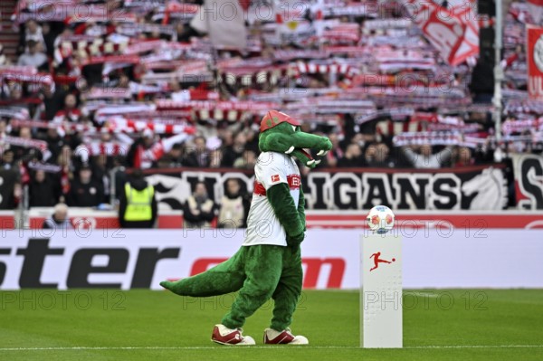 Mascot Fritzle VfB Stuttgart in front of Adidas Derbystar match ball on podium, behind fan block,