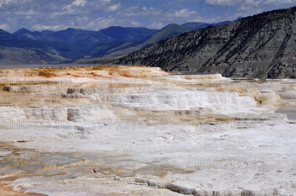 Limestone terraces against mountain backdrop under cloudy sky, Yellowstone National Park, Wyoming,