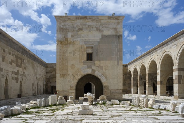 Old courtyard with stone arches and scattered ruins under a clear sky, Sultanhani caravanserai, on
