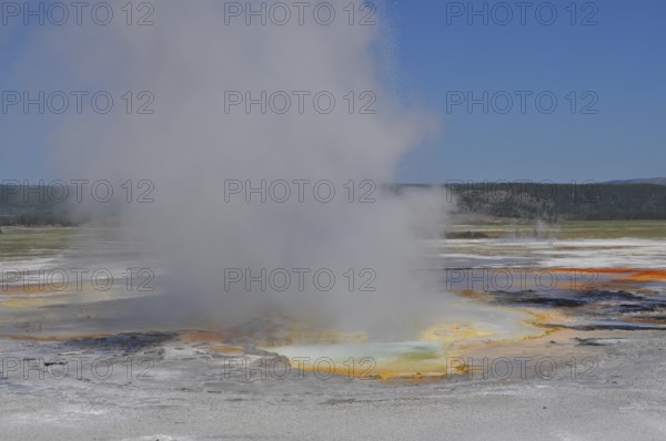 Colorful hot spring with steam under clear skies in a vast natural landscape, Yellowstone National