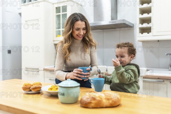 Mother and toddler share a warm morning at the kitchen counter, woman smiling with a mug while the