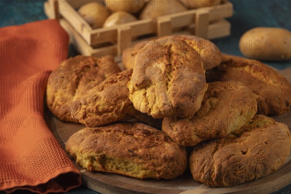 Freshly baked potato rolls with golden brown crust on a wooden board, potatoes in the background
