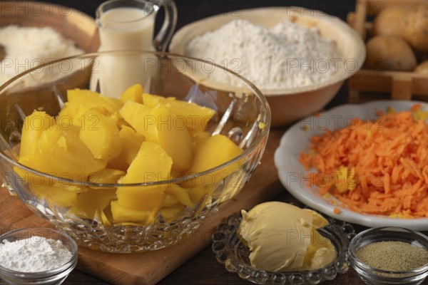 Sliced potatoes and grated carrots next to flour, milk and butter
