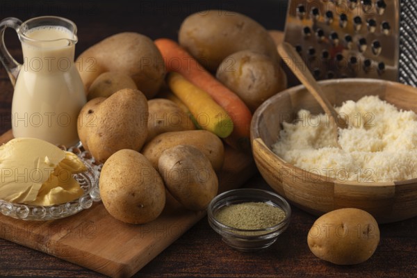 Different ingredients such as potatoes, carrots, parmesan and milk on a kitchen table