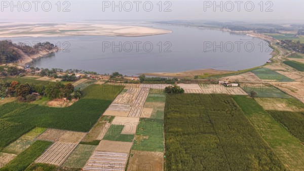 Aerial view of cultivated farmland along the riverbank, with patchwork fields stretching toward a