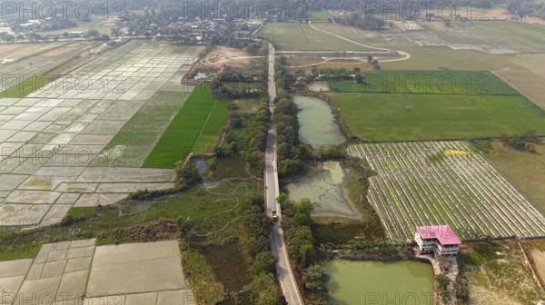 Aerial view of a rural road cutting through patchwork agricultural fields and ponds in the