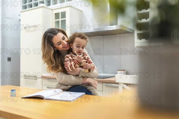 Caring mother smiling and embracing her young child while sitting at a kitchen table, bonding over