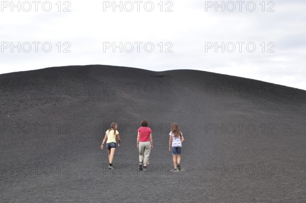 Three people hiking up a trail surrounded by gray lava rock, Craters of the Moon National Monument,