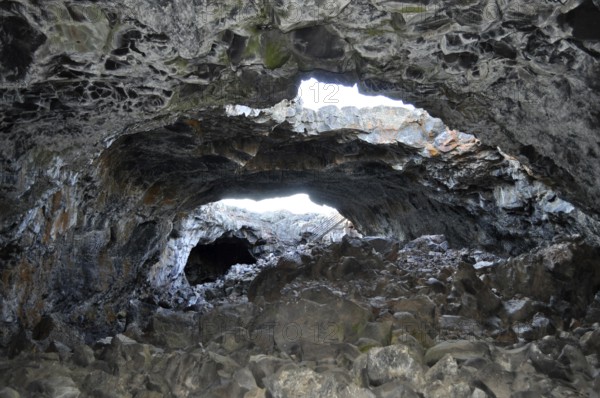 Rocky lava cave opening with irregular walls through which bright light shines in, Craters of the