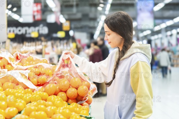 A woman is seen selecting oranges from a fresh produce section in a bustling supermarket, examining
