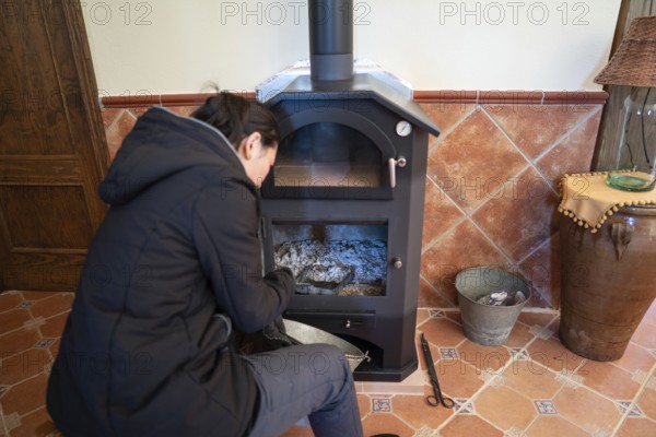 Back view of an Asian woman is cleaning the wood burning stove ashes, preparing it for use, paying
