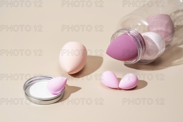 A collection of pink and beige cosmetic sponges arranged on a neutral beige background, ideal for