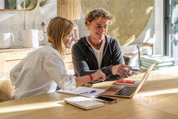 A couple collaborates on a project at home, smiling and engaged They use a laptop and take notes,