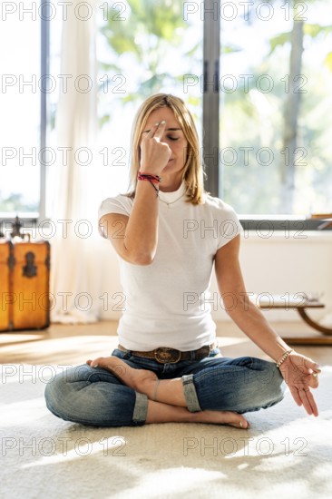 A woman meditates in a cross-legged pose on a carpet, focusing on her breath with a calming hand