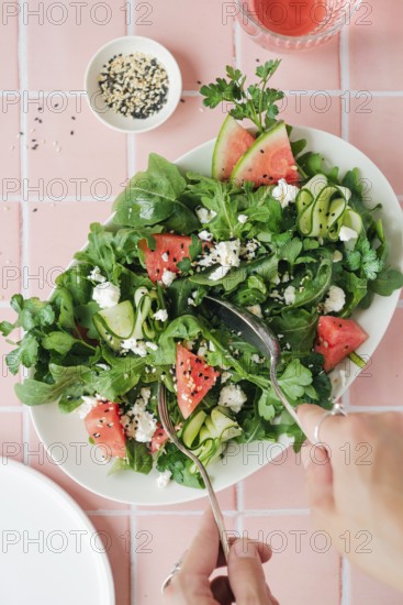 Top view of cropped unrecognizable hands eating vibrant salad featuring ruccola, watermelon,
