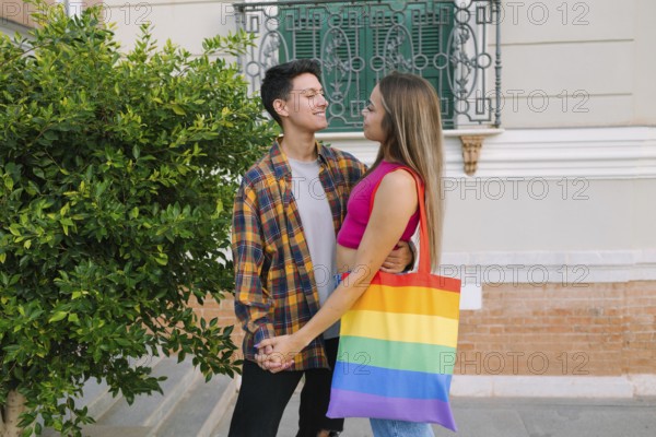 A loving lesbian couple shares a warm embrace while holding hands in an urban setting. One partner