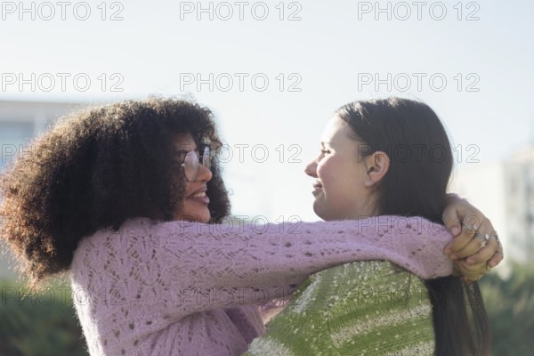 Two friends share a warm embrace in a sunlit park, wearing cozy sweaters. Smiling and enjoying each