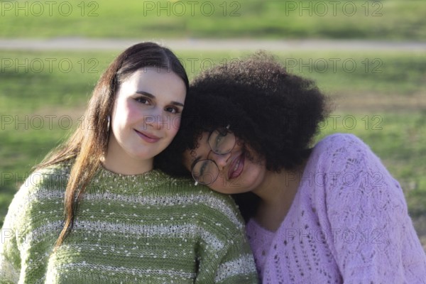Two friends, one with long hair and the other with curly hair and glasses, wearing cozy sweaters,