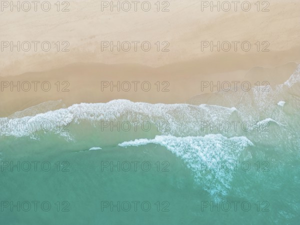 A breathtaking aerial photograph of a sandy beach in Portugal, where gentle turquoise waves meet