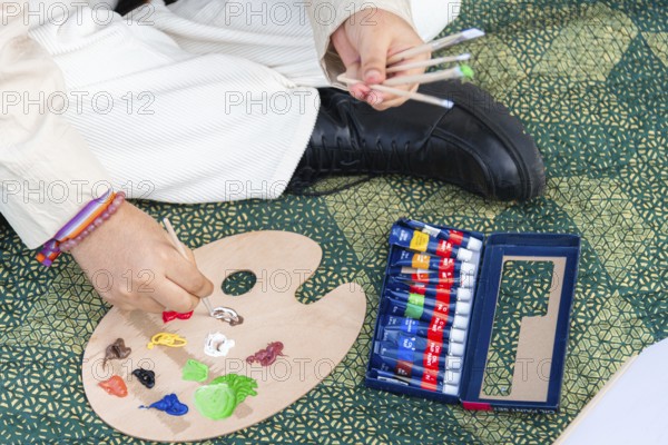 A close up of a young black woman preparing a wooden palette with colorful paint tubes and brushes