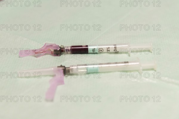 A close-up image of medical syringes filled with blood, laid on a sterile aqua-colored surface,