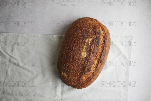 Top view of a freshly baked sourdough bread with a crispy crust, resting on a white linen cloth,