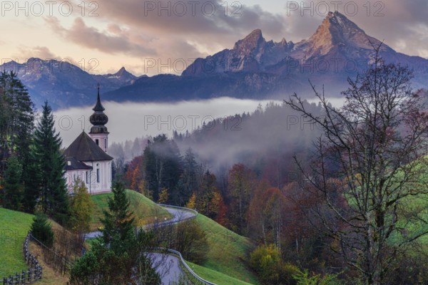 The picturesque Maria Gern Church is nestled among vibrant autumn foliage with the majestic