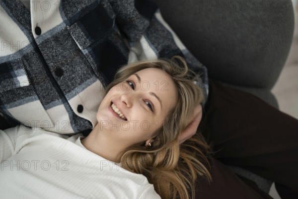 A young woman with a cheerful smile lying next to her cropped unrecognizable partner. She appears