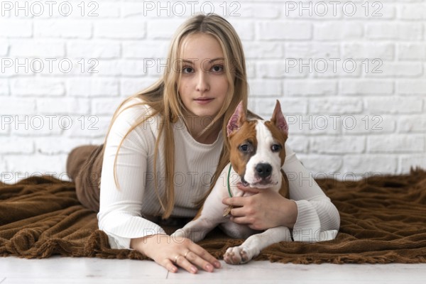 A young woman with blonde hair lounges on a brown blanket, affectionately cuddling her white and