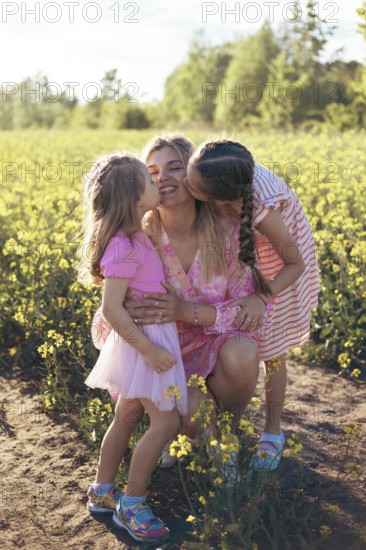 A joyful mother smiles as her daughters kiss her on both cheeks, sharing a tender moment in a